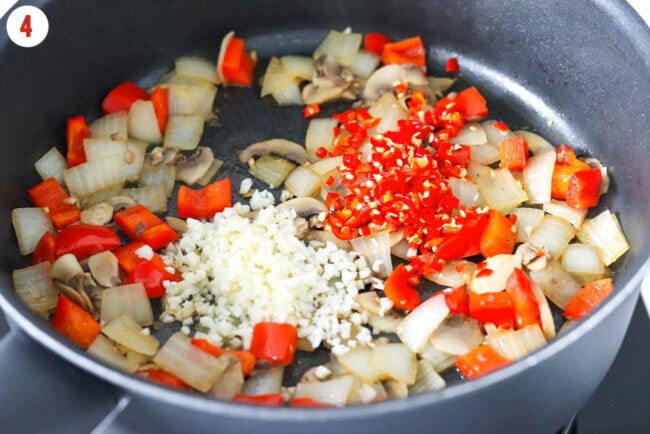 Minced garlic and fresh chilies in a pan with sautéed diced onion, red bell pepper, and sliced mushrooms.
