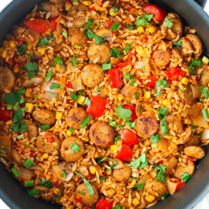 Top view of skillet with chicken sausage and rice with veggies topped with chopped fresh cilantro and green onions.