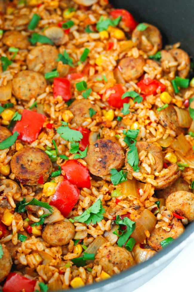 Front view of skillet with chicken sausage and rice with veggies topped with chopped fresh cilantro and green onions.