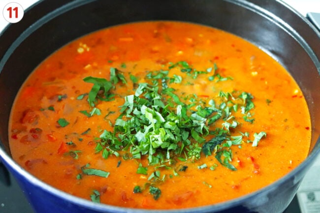 Sliced basil in pot of creamy tomato vodka soup.