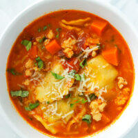 Bowl with spicy ravioli soup with ground chicken topped with grated parmesan and sliced basil.