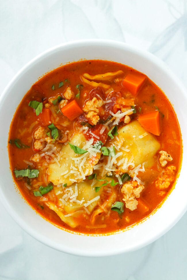 Bowl with spicy ravioli soup with ground chicken topped with grated parmesan and sliced basil.