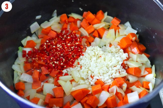 Chopped garlic and red chilies in a pot with sautéed diced onion and carrots.