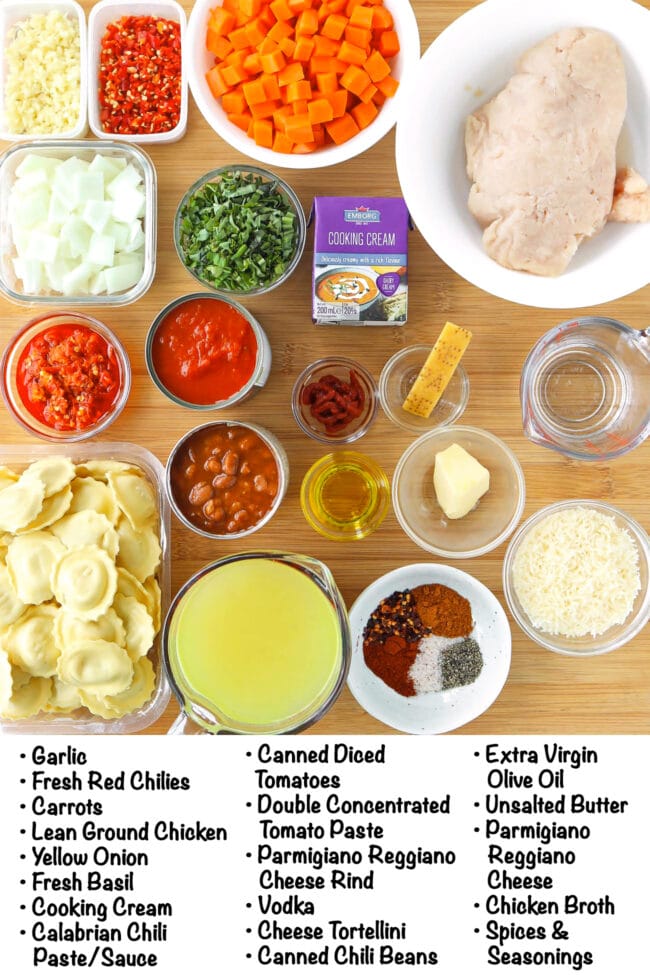 Labeled ingredients for spicy vodka ravioli soup on a wood board.
