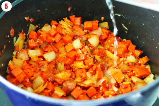 Pouring vodka into pot with sautéed carrots, onion, garlic, red chilies and Calabrian chili paste.