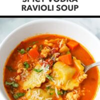 Front view of bowl with spicy ravioli soup topped with grated parmesan and sliced basil. Text overlay "Cozy Comfort Food!" and "Spicy Vodka Ravioli Soup".