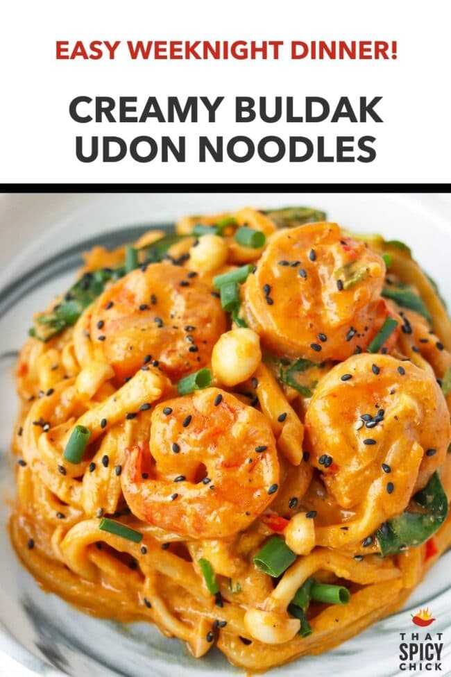 Closeup front view of spicy creamy Korean udon noodles with shrimp on a plate topped with black sesame seeds and green onions. Text overlay "Easy Weeknight Dinner!", "Creamy Buldak Udon Noodles" and "That Spicy Chick".