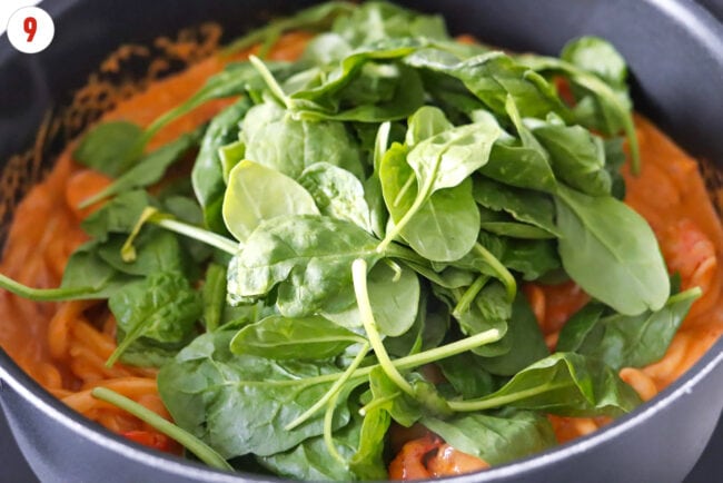 Baby spinach in pan of creamy buldak udon noodles.