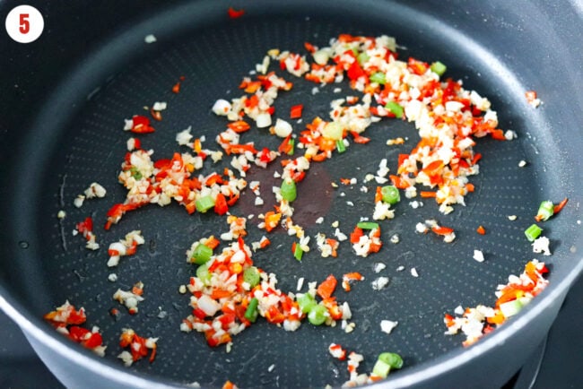 Sautéed garlic, red chilies and green onion white and light green parts in a skillet.