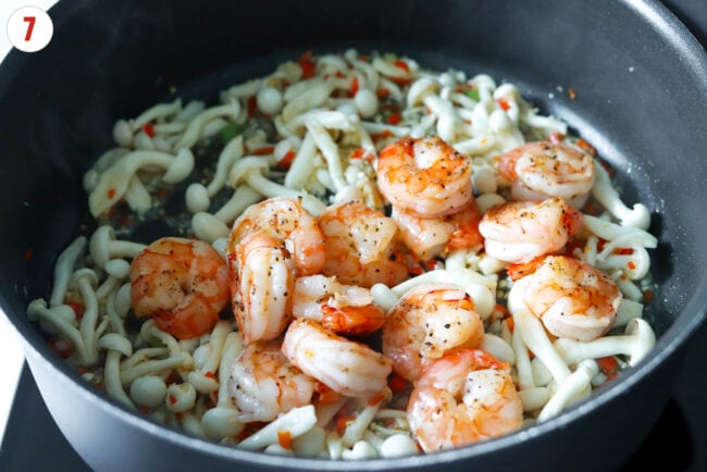 Cooked shrimp in pan with sautéed aromatics and white shimiji mushrooms.