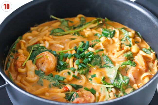Chopped spring onion in pan with creamy buldak udon noodles with shrimp.