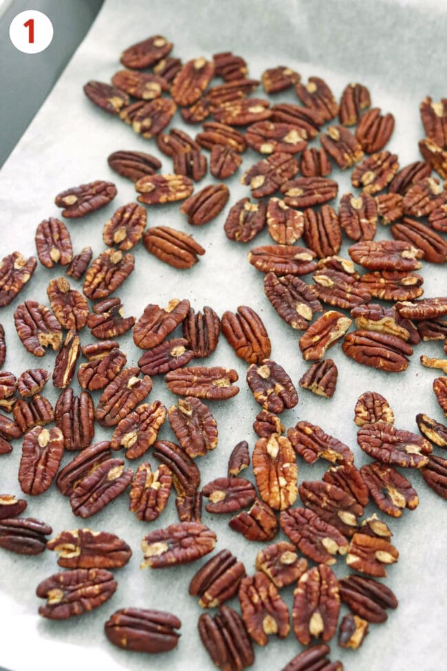 Roasted pecans on a parchment paper lined sheet pan.