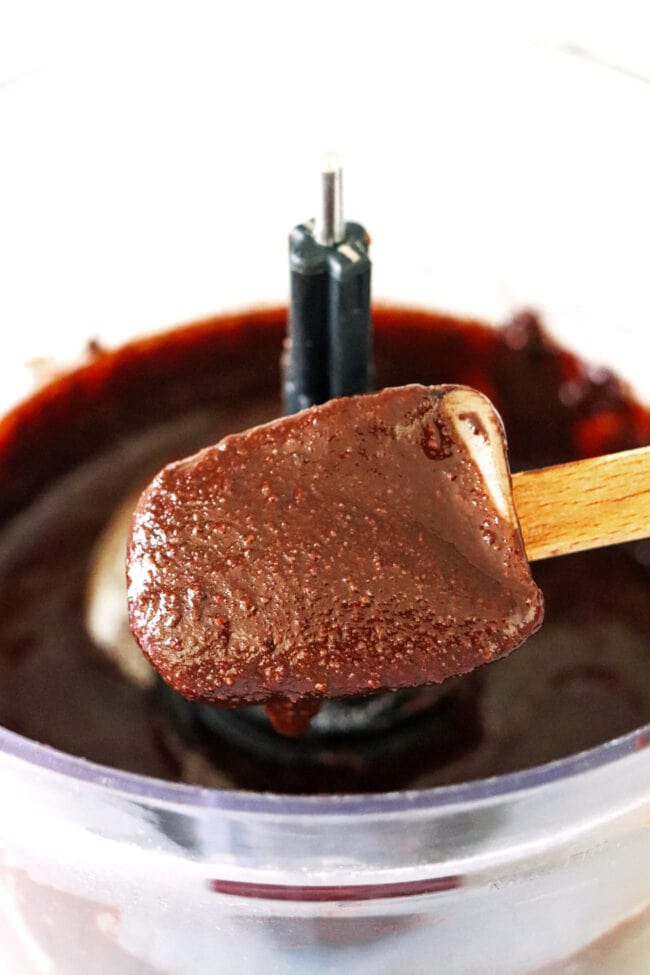 Spatula with dark chocolate pecan butter dripping down into food processor.