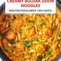 Plate with spicy creamy Korean noodles with shrimp topped with black sesame seeds and green onions. Text overlay "Creamy Buldak Udon Noodles", "High Protein Blended Tofu Sauce!" and "That Spicy Chick".
