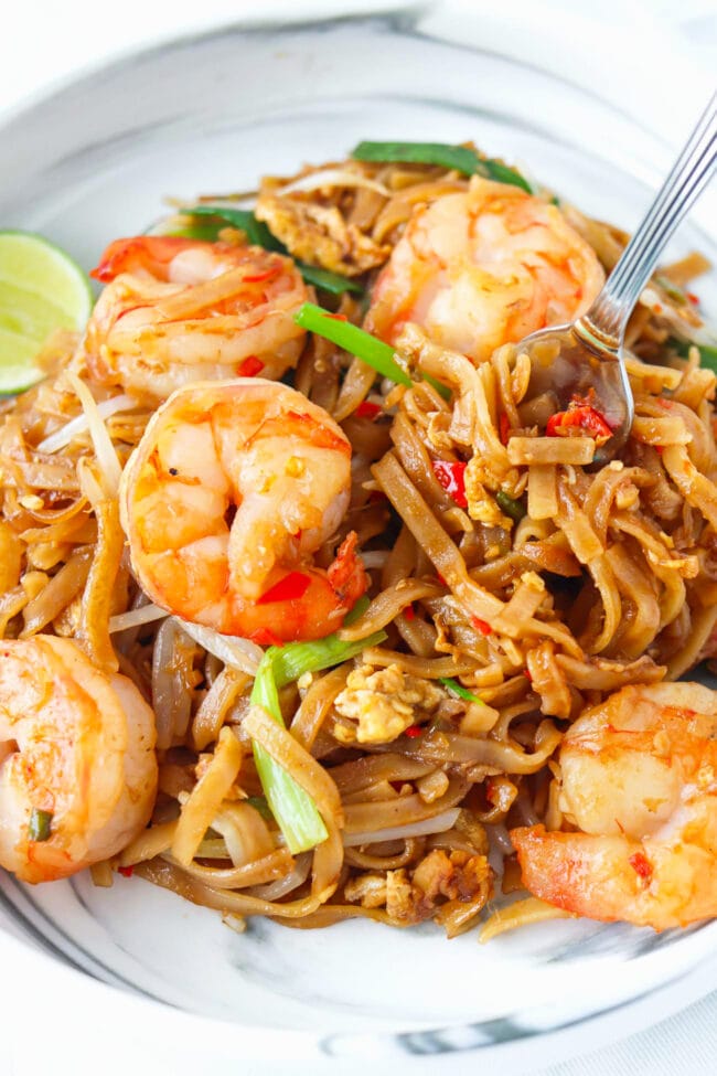 Closeup of fork in plate with spicy Thai rice noodles stir-fry with shrimp.