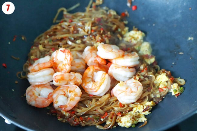 Cooked shrimp on Thai stir-fried rice noodles with chilies and egg in a wok.