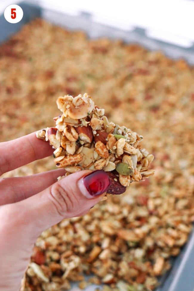 Hand holding up a large granola cluster with almonds.