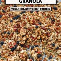 Vanilla almond granola on a baking tray with a spoon. Text overlay "Vanilla Almond Granola", "Vegan | Healthy | High Protein" and "That Spicy Chick".