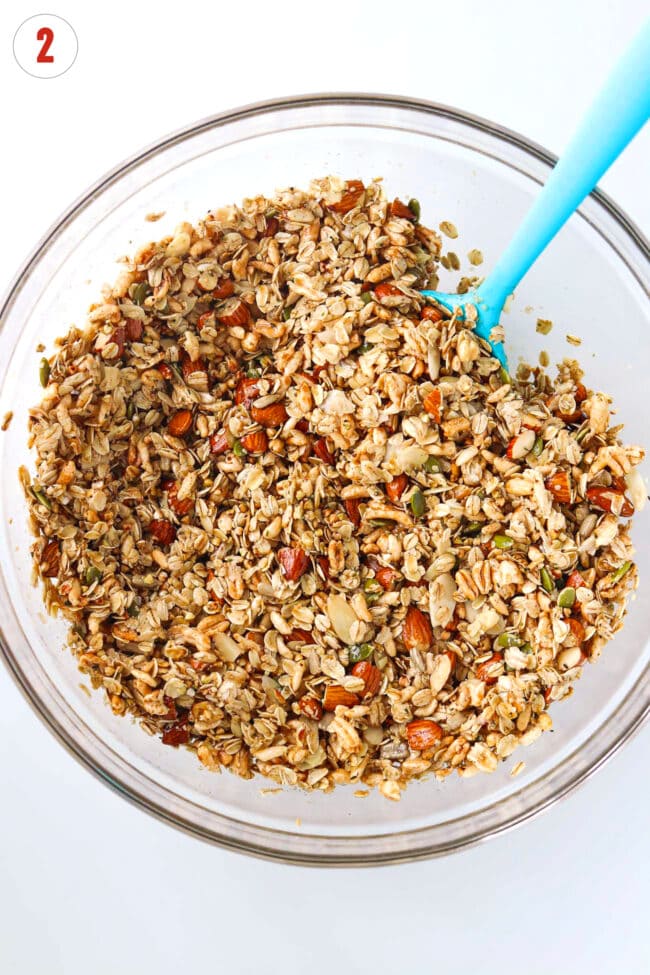 Wet ingredients mixed with dry ingredients for homemade vanilla almond granola in a large mixing bowl.