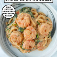 Creamy miso udon noodles with shrimp, spinach and basil on a plate. Text overlay "Cannellini Bean Miso Udon Noodles". "High Protein + High Fiber White Bean Sauce!" and "That Spicy Chick".