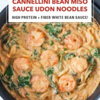 Creamy miso udon noodles with shrimp, spinach and basil in a skillet. Text overlay "Cannellini Bean Miso Sauce Udon Noodles". "High Protein + Fiber White Bean Sauce!" and "That Spicy Chick".