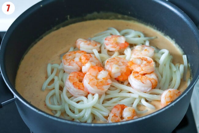 Cooked udon and shrimp added to white bean miso sauce in a pan.