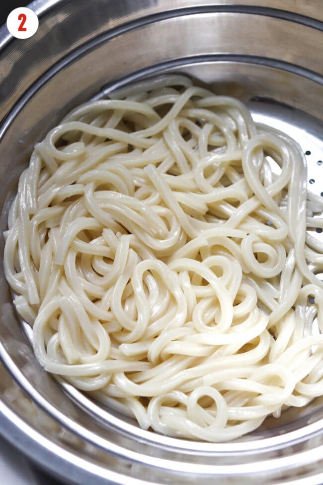 Cooked and drained frozen udon noodles in a colander.