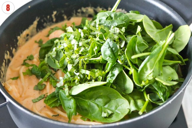 Baby spinach and basil in a pan with creamy white bean sauce udon noodles.