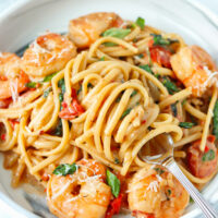 Fork twirled into linguini noodles on a plate with creamy tomato shrimp pasta topped with parmesan and basil.