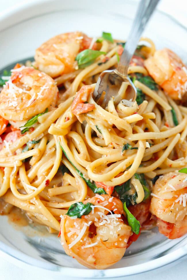 Creamy tomato shrimp pasta on a plate topped with parmesan and basil and a fork twirled into the noodles.