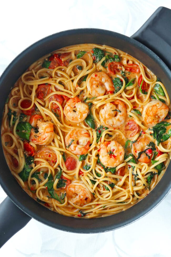 Creamy Tomato Shrimp Pasta with basil, spinach and cherry tomatoes in a skillet.
