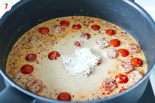 Added grated Parmigiano Reggiano cheese to creamy cherry tomato sauce in a skillet.