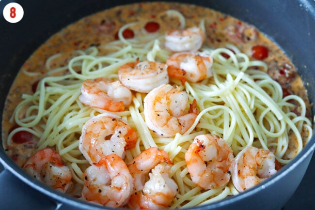 Cooked linguini and seared shrimp in a skillet with creamy tomato garlic butter sauce.