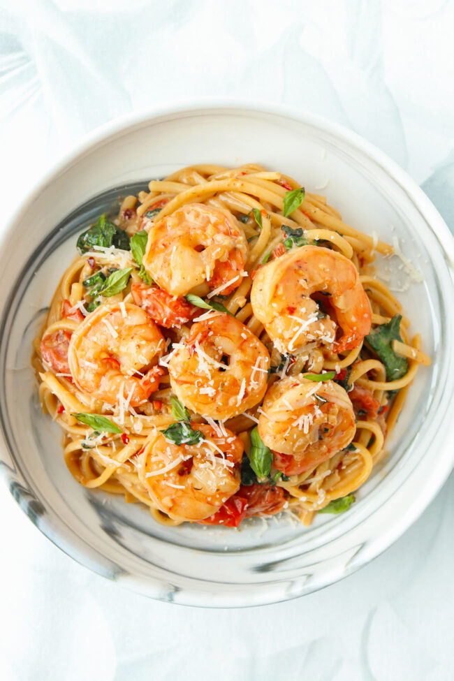 Plate with creamy tomato shrimp pasta with cherry tomatoes, spinach, and basil topped with grated parmesan.