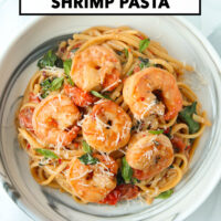 Plate with cream sauce shrimp pasta with cherry tomatoes, garlic, spinach, basil topped with Parmigiano Reggiano cheese. Text overlay "Creamy Tomato Shrimp Pasta", and "That Spicy Chick".