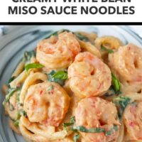 Front view of creamy miso udon noodles with shrimp, spinach and basil on a plate. Text overlay "High Protein Dinner!", "Creamy White Bean Miso Sauce Udon Noodles" and "That Spicy Chick".