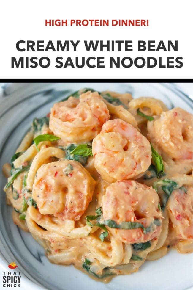 Front view of creamy miso udon noodles with shrimp, spinach and basil on a plate. Text overlay "High Protein Dinner!", "Creamy White Bean Miso Sauce Udon Noodles" and "That Spicy Chick".