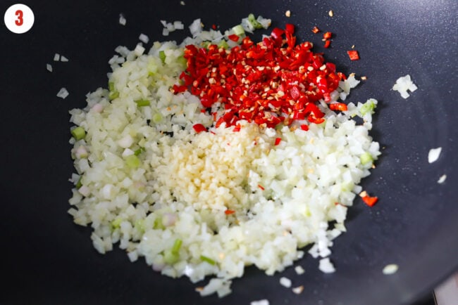 Minced garlic and red chilies added to wok with stir-fried onions and ginger.