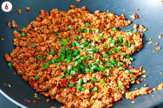 Chopped green onions added to wok with Korean chicken stir-fry.