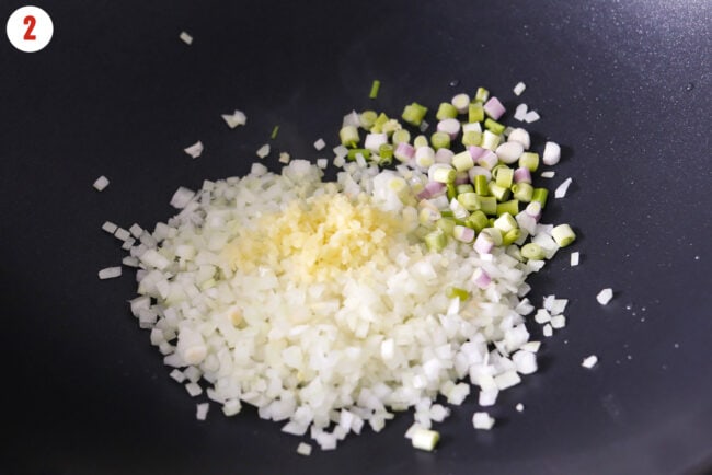Finely chopped yellow onion, spring onion white and light green parts, and minced ginger in a wok.