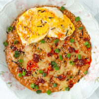 Closeup of plate with savory oats with kimchi topped with a fried egg, chili crisp, furikake and green onions.