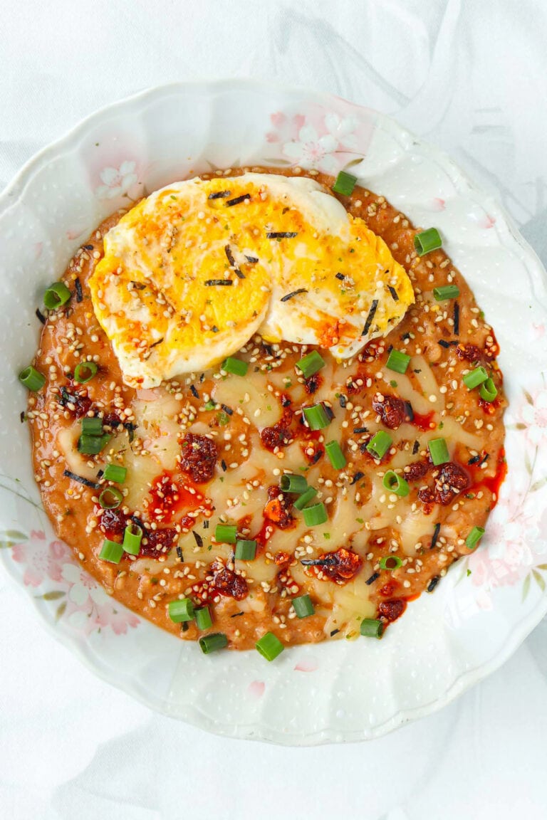 Closeup of plate with savory oats with kimchi topped with a fried egg, chili crisp, furikake and green onions.