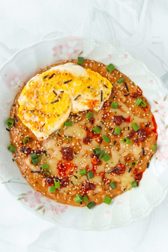 Plate with savory oats topped with a fried egg, chili crisp, furikake and green onions.