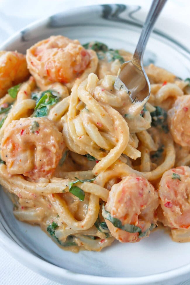 Fork in plate with chili oil white bean miso sauce udon noodles with shrimp.