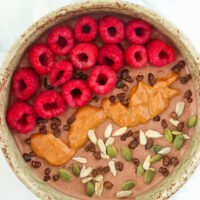 Chocolate overnight oats bowl topped with raspberries, seeds, cacao nibs and peanut butter.