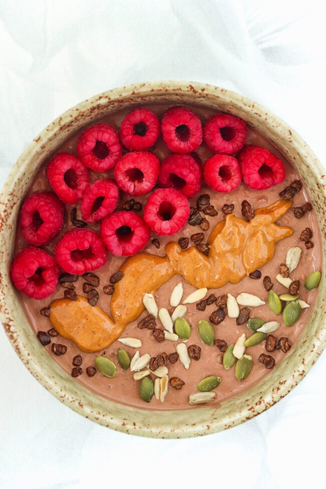 Chocolate overnight oats bowl topped with raspberries, seeds, cacao nibs and peanut butter.