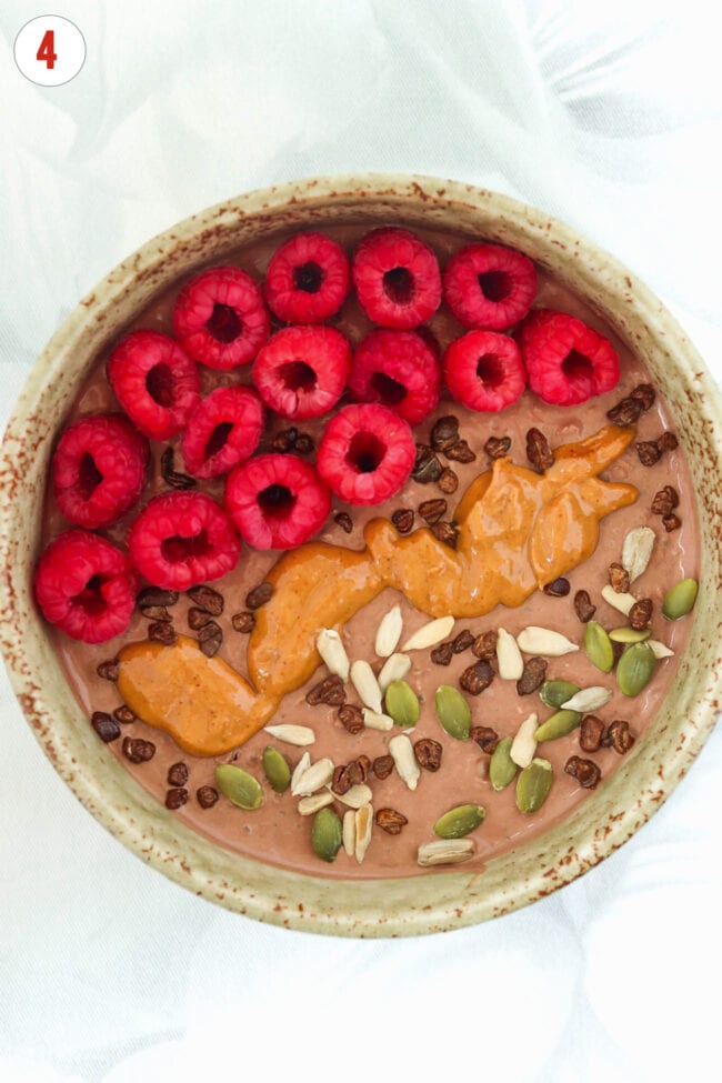 High protein chocolate overnight oats bowl topped with raspberries, seeds, cacao nibs and peanut butter.
