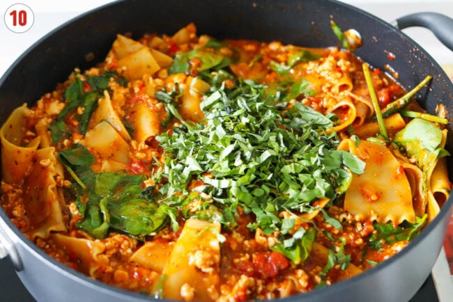 Sliced basil in pan with red pesto lasagna with cottage cheese.