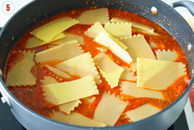 Broken up lasagna noodles in a skillet with red pesto tomato sauce.