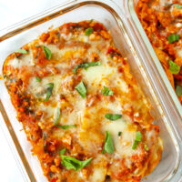 Red pesto chicken skillet lasagna in meal prep containers garnished with basil.